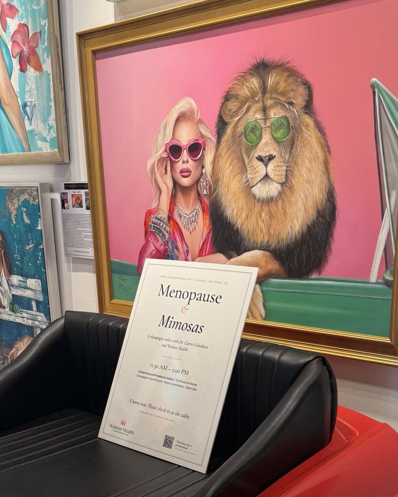 The Menopause & Mimosas welcome sign resting on a red vintage-car bench beneath a painting of a woman and a lion